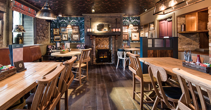 view of the dining area inside The Seaton Lane Inn with collection of wooden tables and chairs and patterned wallpaper on walls.